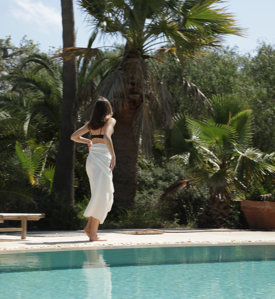 Woman standing with a towel by a pool with palm trees in the background
